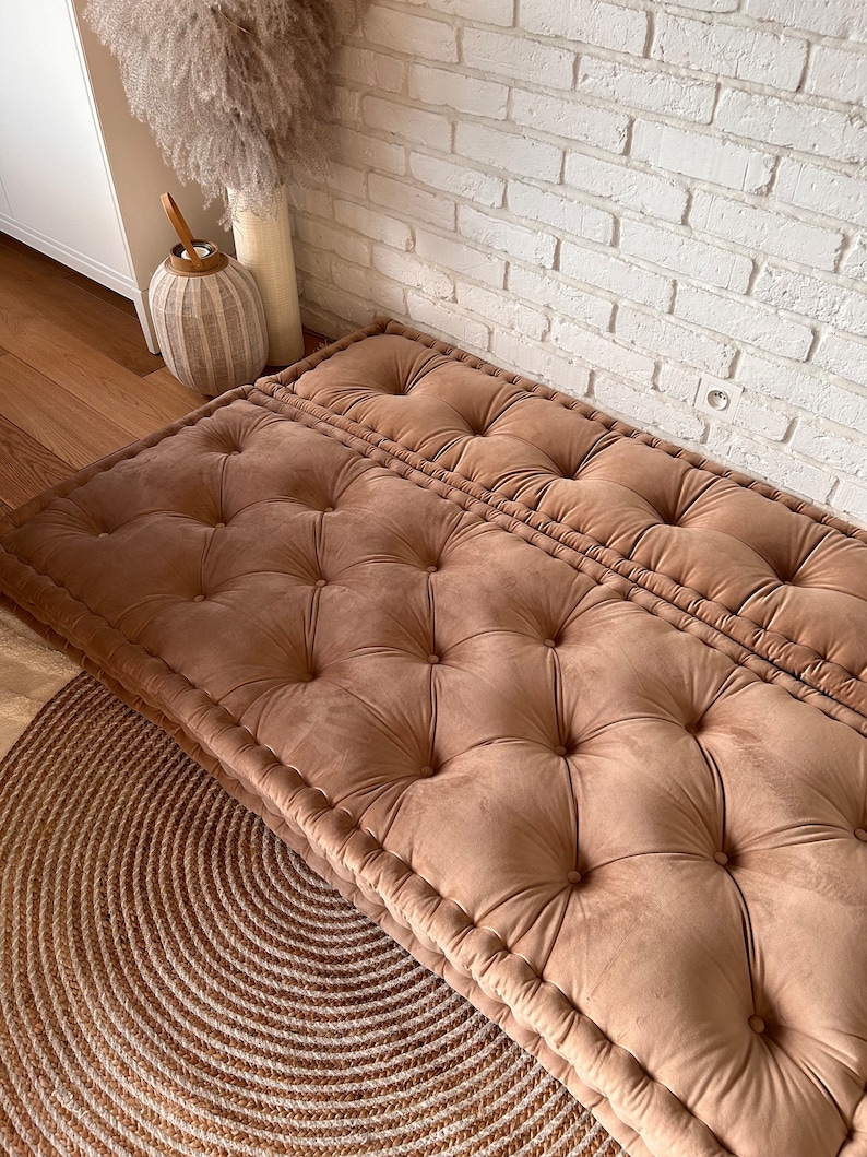 May include: A brown tufted floor cushion with a button-tufted design. The cushion is made of a soft, plush fabric and is perfect for adding a touch of comfort and style to any room.