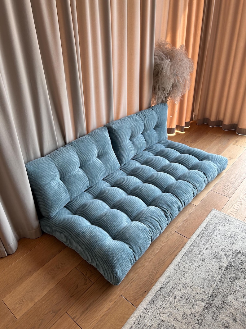 May include: A blue corduroy floor cushion with tufted buttons. The cushion is made up of two separate pieces that can be used as a sofa or a bed.
