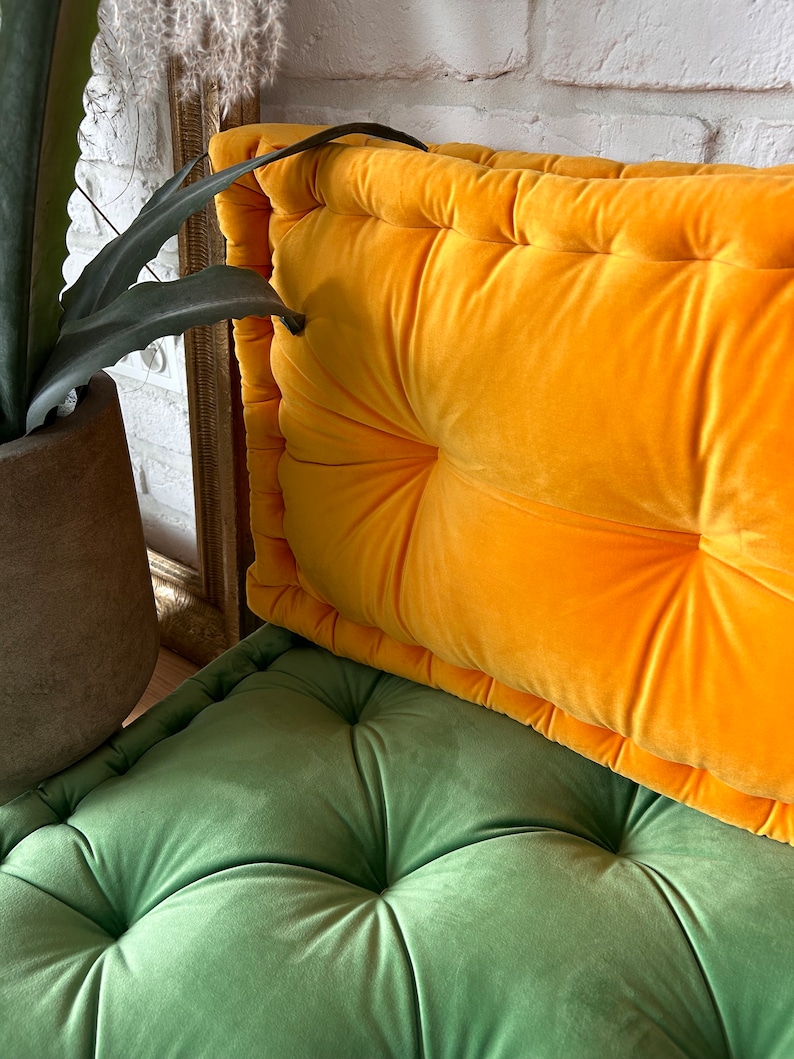 May include: A bright yellow velvet cushion with button tufting sits on top of a green velvet cushion with button tufting. Both cushions have a soft, plush texture.