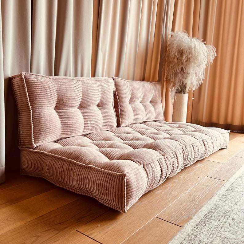 May include: A pink corduroy floor cushion with tufted buttons and a matching back cushion. The cushion is made of soft, plush fabric and is perfect for lounging or sitting on the floor.