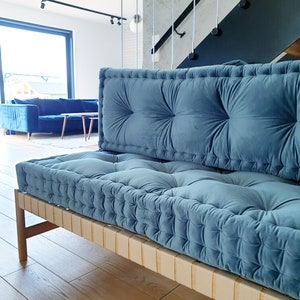 May include: A blue velvet tufted sofa with a wooden frame and a natural woven base. The sofa is in a modern living room with a wooden floor.