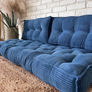 May include: A blue corduroy floor cushion with tufted buttons and a matching back cushion. The cushion is on a woven rug.