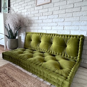 Peut inclure: Un grand coussin de sol vert touffu avec une base &eacute;paisse et rembourr&eacute;e. Le coussin est en velours et pr&eacute;sente un design capitonn&eacute;. Le coussin est pos&eacute; sur un tapis tiss&eacute;.