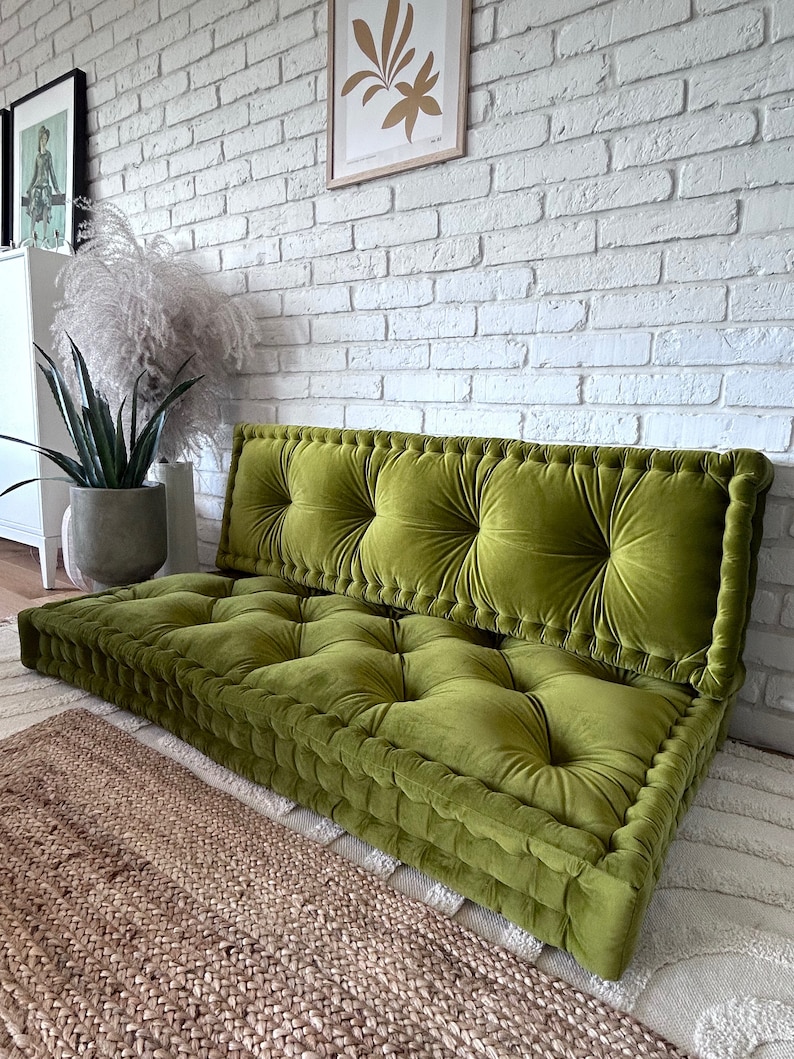 Peut inclure: Un grand coussin de sol vert touffu avec une base &eacute;paisse et rembourr&eacute;e. Le coussin est en velours et pr&eacute;sente un design capitonn&eacute;. Le coussin est pos&eacute; sur un tapis tiss&eacute;.