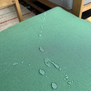 May include: A close-up of a green fabric surface with water droplets on it. The fabric has a textured weave.