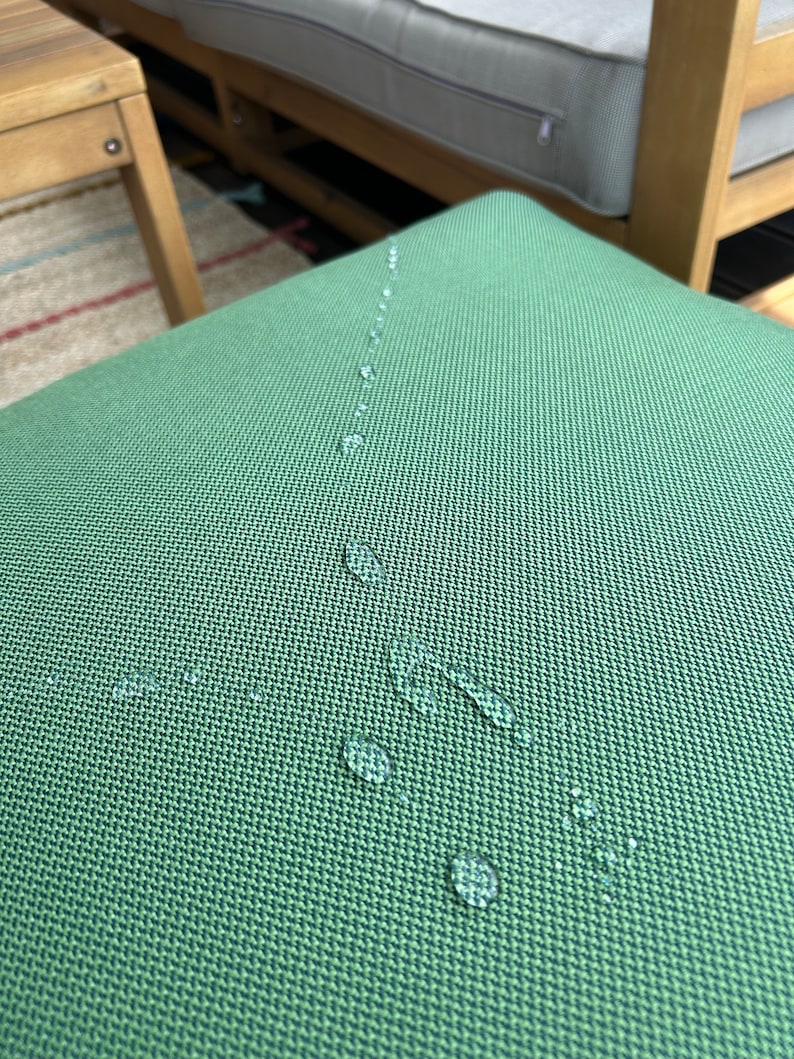 May include: A close-up of a green fabric surface with water droplets on it. The fabric has a textured weave.