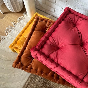 Peut inclure: Trois coussins de sol carr&eacute;s dans diff&eacute;rentes nuances de rouge, orange et jaune. Les coussins sont en velours et ont un design capitonn&eacute;.