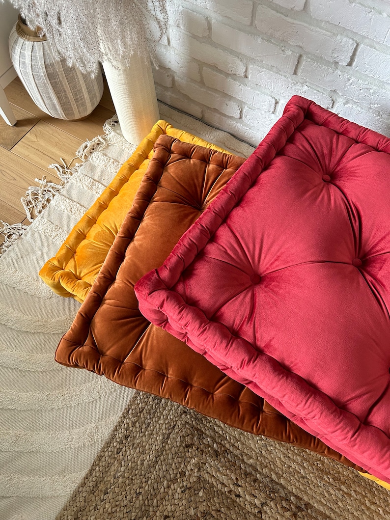 Peut inclure: Trois coussins de sol carr&eacute;s dans diff&eacute;rentes nuances de rouge, orange et jaune. Les coussins sont en velours et ont un design capitonn&eacute;.