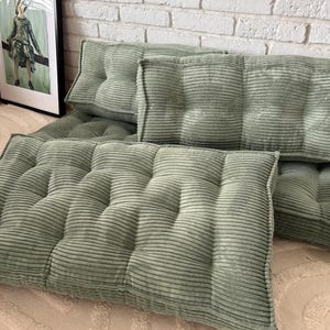 May include: A set of five sage green corduroy floor cushions with button tufting. The cushions are arranged in a row on a light beige rug.
