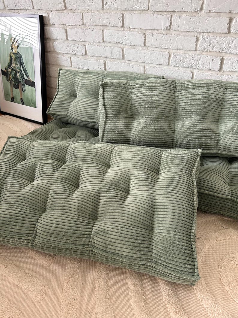 May include: A set of five sage green corduroy floor cushions with button tufting. The cushions are arranged in a row on a light beige rug.