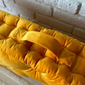 Peut inclure: Un coussin de sol en velours jaune moutarde avec un design capitonn&eacute; et une poign&eacute;e sur le dessus.