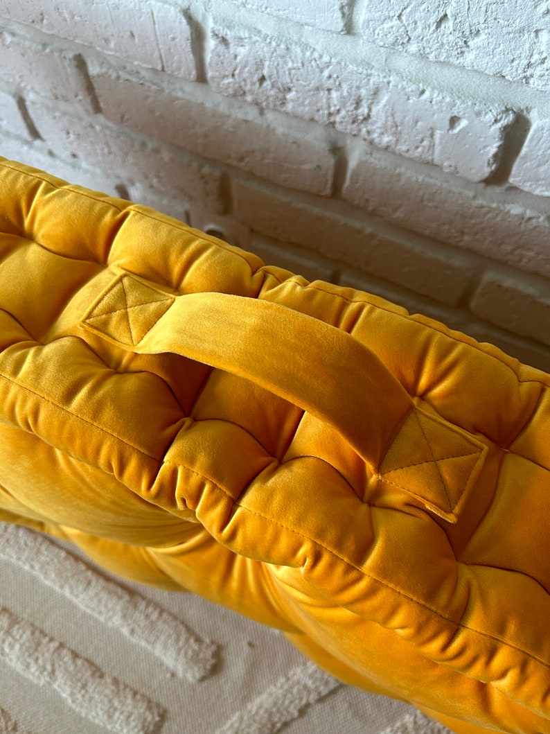 Peut inclure: Un coussin de sol en velours jaune moutarde avec un design capitonn&eacute; et une poign&eacute;e sur le dessus.