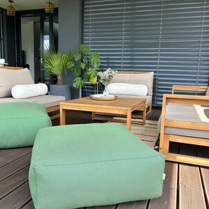 May include: Green outdoor patio furniture with a wooden coffee table and two green poufs. The furniture is on a wooden deck.