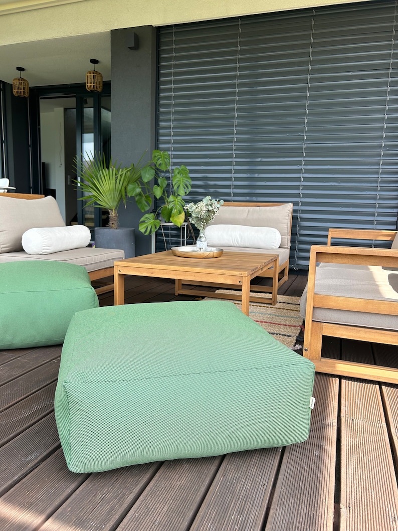 May include: Green outdoor patio furniture with a wooden coffee table and two green poufs. The furniture is on a wooden deck.