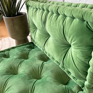 May include: A green velvet floor cushion with tufted buttons and a piped edge. The cushion is made of soft, plush fabric and is perfect for adding a touch of comfort and style to any room.