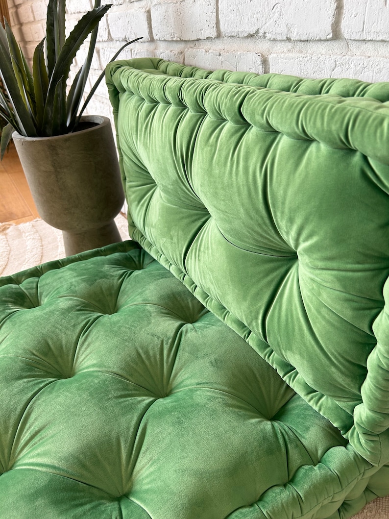 May include: A green velvet floor cushion with tufted buttons and a piped edge. The cushion is made of soft, plush fabric and is perfect for adding a touch of comfort and style to any room.