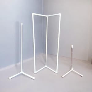 Op de afbeelding: Drie witte metalen standaards, twee zijn driepotig en één is een rechthoekig frame met drie poten. De standaards zijn gemaakt van dunne metalen buizen.