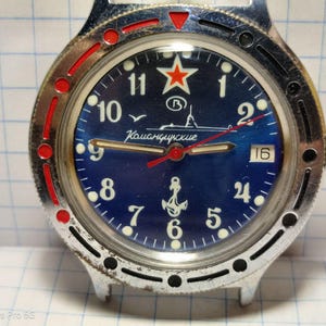 May include: A vintage wristwatch with a blue face featuring white numerals, a red star, and the text "Командирские". The watch has a silver-colored bezel with red accents and a date display at the 3 o'clock position.