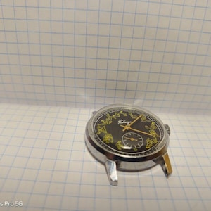 May include: A vintage wristwatch with a black face and gold hands and markers. The watch has a silver-colored metal case and a small subdial. The face features the word "Победа" in gold lettering.