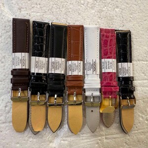 May include: A collection of eight watch straps in various colors and textures. The straps include shades of brown, black, white, and pink, with some featuring a crocodile skin pattern. Each strap has a silver buckle and the text "NAGATA GENUINE LEATHER SPAIN".