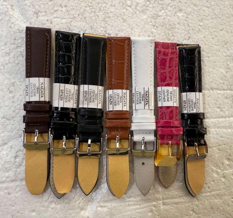 May include: A collection of eight watch straps in various colors and textures. The straps include shades of brown, black, white, and pink, with some featuring a crocodile skin pattern. Each strap has a silver buckle and the text "NAGATA GENUINE LEATHER SPAIN".