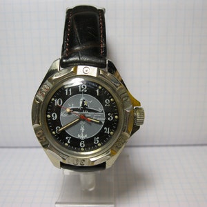 Puede incluir: Un reloj de pulsera negro y plateado con una correa de cuero negro. La esfera del reloj presenta un gráfico de submarino y el texto "Капитан Батискаф".