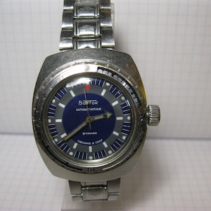 May include: A silver wristwatch with a blue face and white markings. The watch has a stainless steel band and says "Восток антимагнитные" and "Сделано в СССР" on the face.