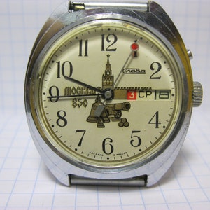 May include: A silver wristwatch with a white face and black numbers. The watch face features a depiction of the Kremlin and the text "Moscow 850". The date window displays "3 CPI 8".
