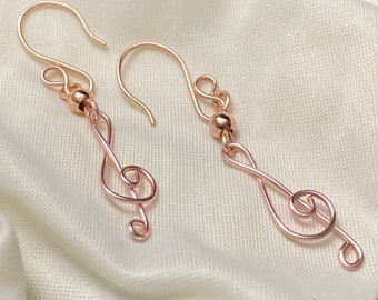 Op de afbeelding: Een paar oorbellen van roségoud in de vorm van vioolsleutels. Elke oorbel heeft een kleine ronde kraal bovenop de vioolsleutel.