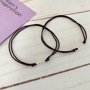 May include: Two brown string bracelets with silver beads. Each bracelet has a row of five silver beads.