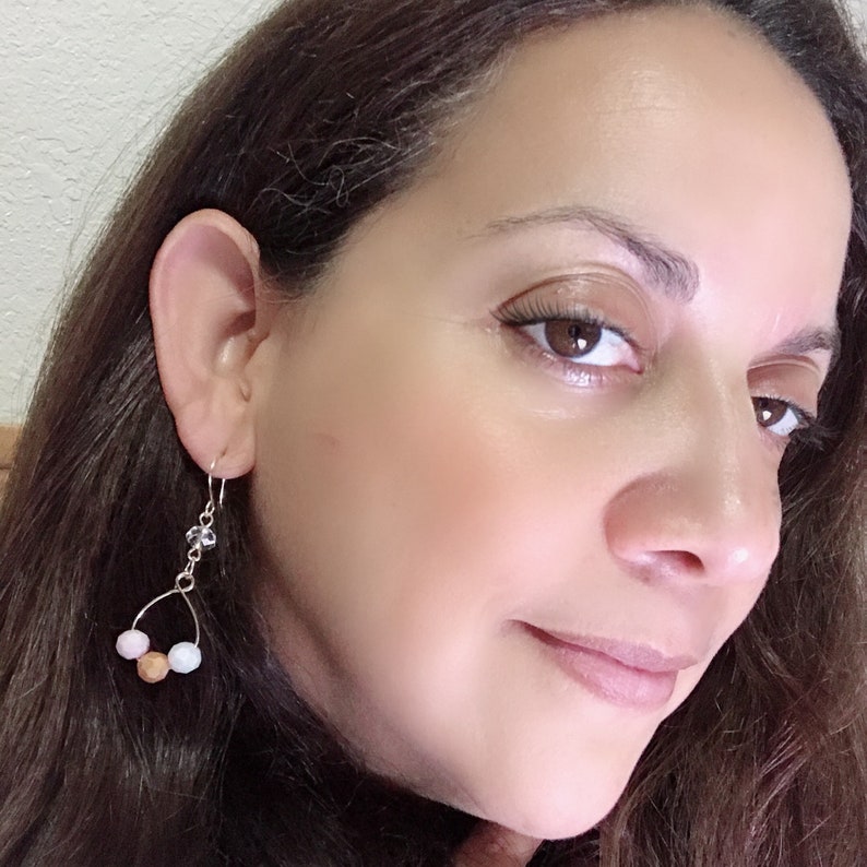 May include: A pair of silver dangle earrings with a teardrop-shaped crystal charm and three round beads in pink, white, and brown.