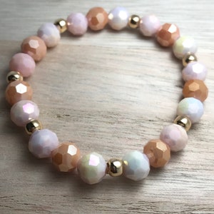 May include: A bracelet made of faceted glass beads in shades of peach, pink, and white, separated by gold-toned spacers.