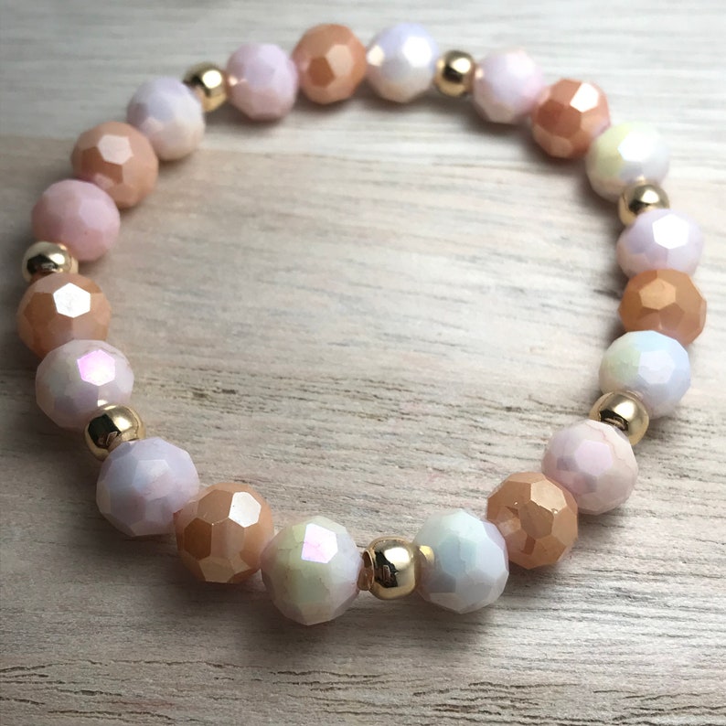 May include: A bracelet made of faceted glass beads in shades of peach, pink, and white, separated by gold-toned spacers.