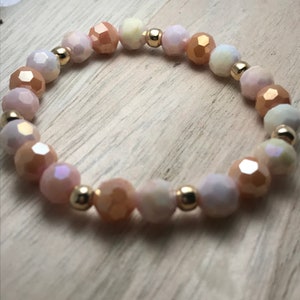 May include: A delicate bracelet made with iridescent glass beads in shades of peach, white, and cream. The beads are separated by small gold spacers.
