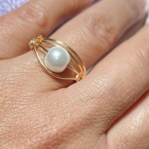 May include: A gold wire ring with a single white pearl in the center.