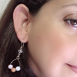 May include: Silver dangle earrings with a crystal charm and three pastel-colored beads. The beads are pink, brown, and blue.