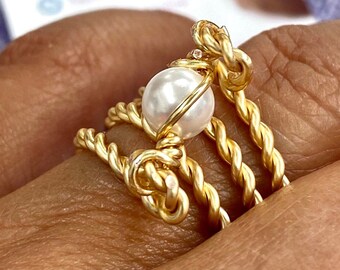 May include: A gold wire ring with a white pearl in the centre. The wire is twisted and forms a knot at the top of the ring.