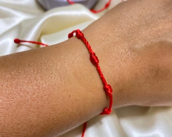 May include: A red string bracelet with multiple knots. The bracelet is tied around a person's wrist.