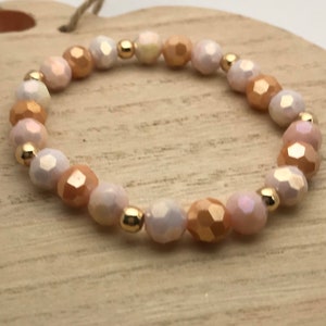 May include: A delicate bracelet made with iridescent white and peach-colored faceted beads and gold-toned spacers.