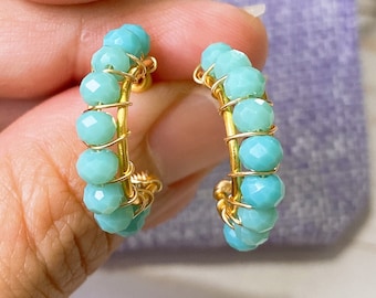 May include: A pair of gold hoop earrings with turquoise blue beads. The earrings are made with wire wrapped around the beads.