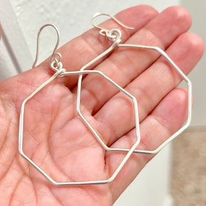 May include: A pair of silver octagon hoop earrings. The earrings are made of thin wire and have a simple, geometric design.