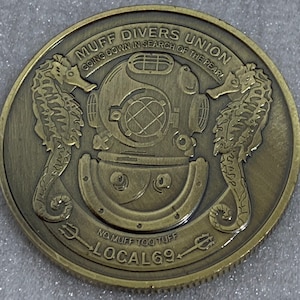 May include: A gold-colored metal coin with the words "Muff Divers Union" and "Going Down in Search of the Pearl" around the rim. The center of the coin features a diving helmet with two seahorses on either side. The bottom of the coin reads "No Muff Too Tuff" and "Local 69".