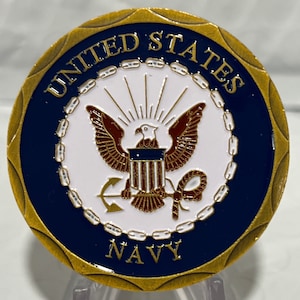 May include: A round, gold-colored coin with a navy blue border. The coin features the words "UNITED STATES NAVY" and a central emblem of an eagle, anchor, and shield in brown, white, and gold.