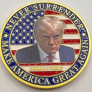 May include: Gold-colored coin with a portrait of Donald J. Trump in the center. The coin features the American flag in the background and the text "Make America Great Again" and "Never Surrender" around the edge.