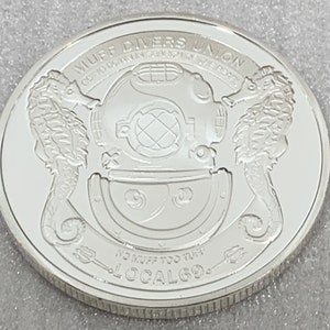 May include: Silver coin with a diving helmet, two seahorses, and the text "Muff Divers Union" and "No Muff Too Tuff Local 69".
