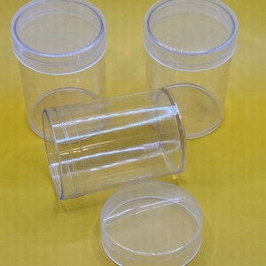 May include: Four clear plastic containers with lids. The containers are cylindrical and have a smooth, shiny finish. The lids are round and fit snugly on top of the containers.