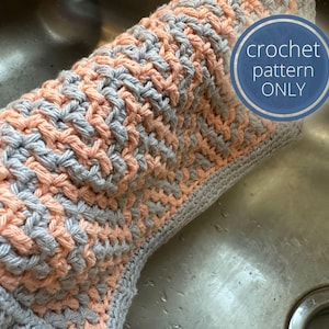 May include: A close-up of a crocheted dishcloth in gray and peach colors. The dishcloth is made with a simple stitch pattern and is lying in a stainless steel sink. The text "crochet pattern ONLY" is visible in a blue circle.