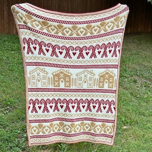 May include: A white, red, and gold crochet blanket with a gingerbread house and candy cane pattern.