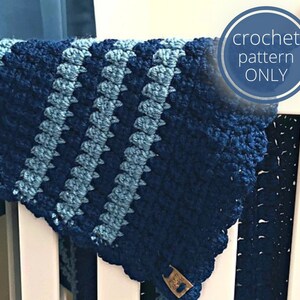 May include: A crochet baby blanket in shades of blue with a striped pattern. The blanket is draped over a white crib.