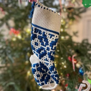 Op de afbeelding: Een witte gehaakte kerstsok met een blauw sneeuwvlokkenpatroon.